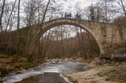 an old bridge over the river with a group of people on it